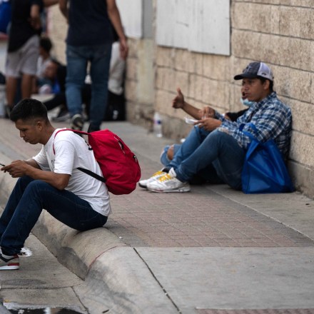 Migrants that arrived from Mexico look at their phones as they wait for transportation near a processing center, in Brownsville, Texas on May 10, 2023. The US on May 11, 2023, will officially end its 40-month Covid-19 emergency, also discarding the Title 42 law, a tool that has been used to prevent millions of migrants from entering the country. (Photo by ANDREW CABALLERO-REYNOLDS / AFP) (Photo by ANDREW CABALLERO-REYNOLDS/AFP via Getty Images)