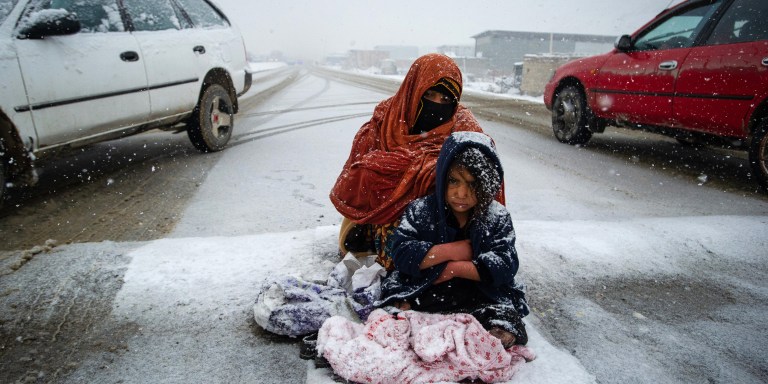 PUL-E ALAM, AFGHANISTAN -- JANUARY 17: An Afghan woman begs for money from passing cars in the snow, with her child huddled beside her, on the Kabul road south to Pul-e Alam, Afghanistan, on January 17, 2022. The UN World Food Program warns that 98% of Afghans are not getting enough to eat, due to a severe drought, the onset of winter, and the collapse of the economy and and freezing of Afghan and donor funds after the Taliban takeover of the country in August, 2021. The UN has made an emergency appeal for $5.5 billion to feed the hungry and forestall further economic collapse. (Photo by Scott Peterson/Getty Images)