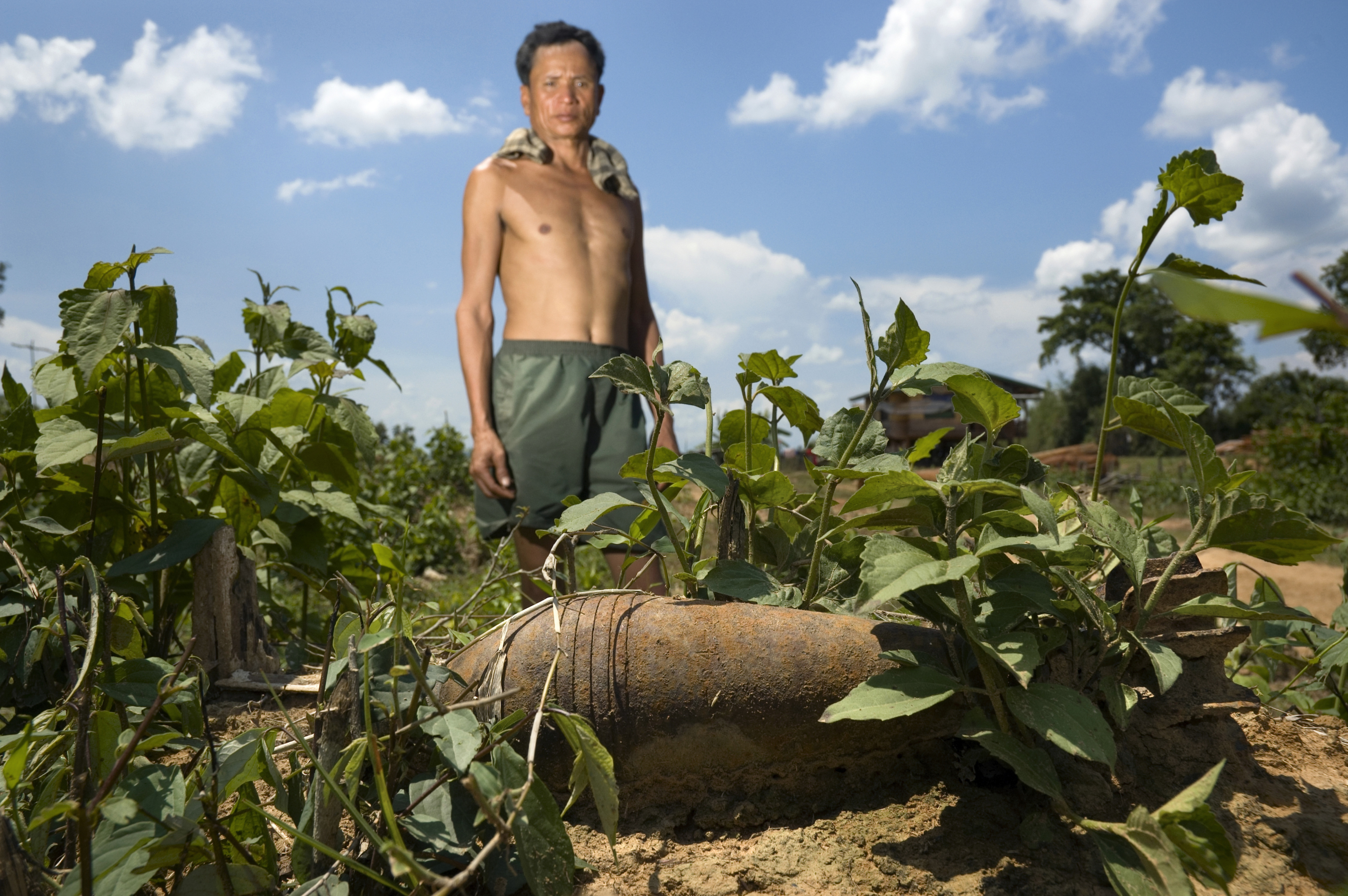 A farmer stands behind a live mortar he found in the field behind his home in Laos, near a branch of the former Ho Chi Minh Trail.