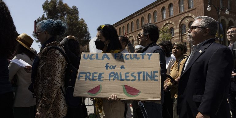 A demonstrator holds a poster reading "UCLA Faculty for a Free Palestine" as UCLA faculty and staff members demonstrate next to the pro-Palestinian encampment on the campus of the University of California, Los Angeles (UCLA) in Los Angeles, California, on May 1, 2024. Dozens of police cars patrolled at the University of California, Los Angeles campus in response to violent clashes overnight when counter-protesters attacked an encampment of pro-Palestinian students. (Photo by Etienne LAURENT / AFP) (Photo by ETIENNE LAURENT/AFP via Getty Images)