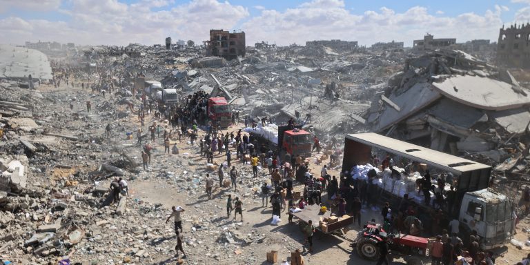 Palestinians rally around aid trucks which entered from the Karem Abu Salem crossing, in Khan Yunis in the southern Gaza Strip on October 12, 2025, as a ceasefire between Israel and Palestinian factions holds in the besieged territory. A Gaza ceasefire was holding for a third day on October 12, ahead of a US-proposed hostage-prisoner exchange and a summit aimed at charting a path to peace after two years of war. (Photo by Omar AL-QATTAA / AFP) (Photo by OMAR AL-QATTAA/AFP via Getty Images)