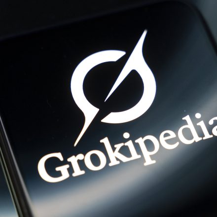 The Grokipedia encyclopedia logo appears on a smartphone screen reflecting an abstract illustration. The encyclopedia is entirely generated by Grok AI and is intended to be an alternative to Wikipedia, according to Elon Musk, in Creteil, France, on October 29, 2025. (Photo by Samuel Boivin/NurPhoto via Getty Images)