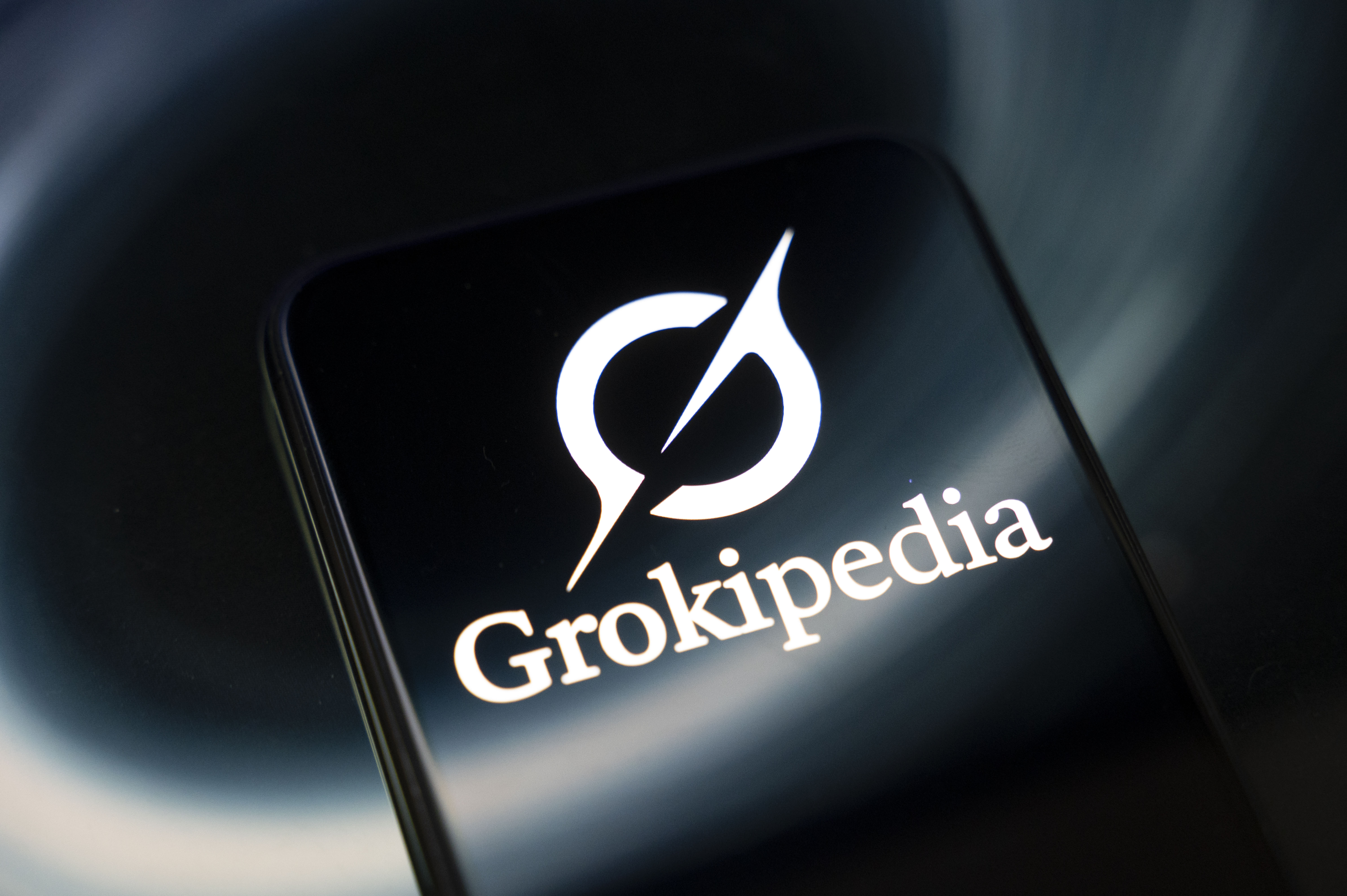The Grokipedia encyclopedia logo appears on a smartphone screen reflecting an abstract illustration. The encyclopedia is entirely generated by Grok AI and is intended to be an alternative to Wikipedia, according to Elon Musk, in Creteil, France, on October 29, 2025. (Photo by Samuel Boivin/NurPhoto via Getty Images)