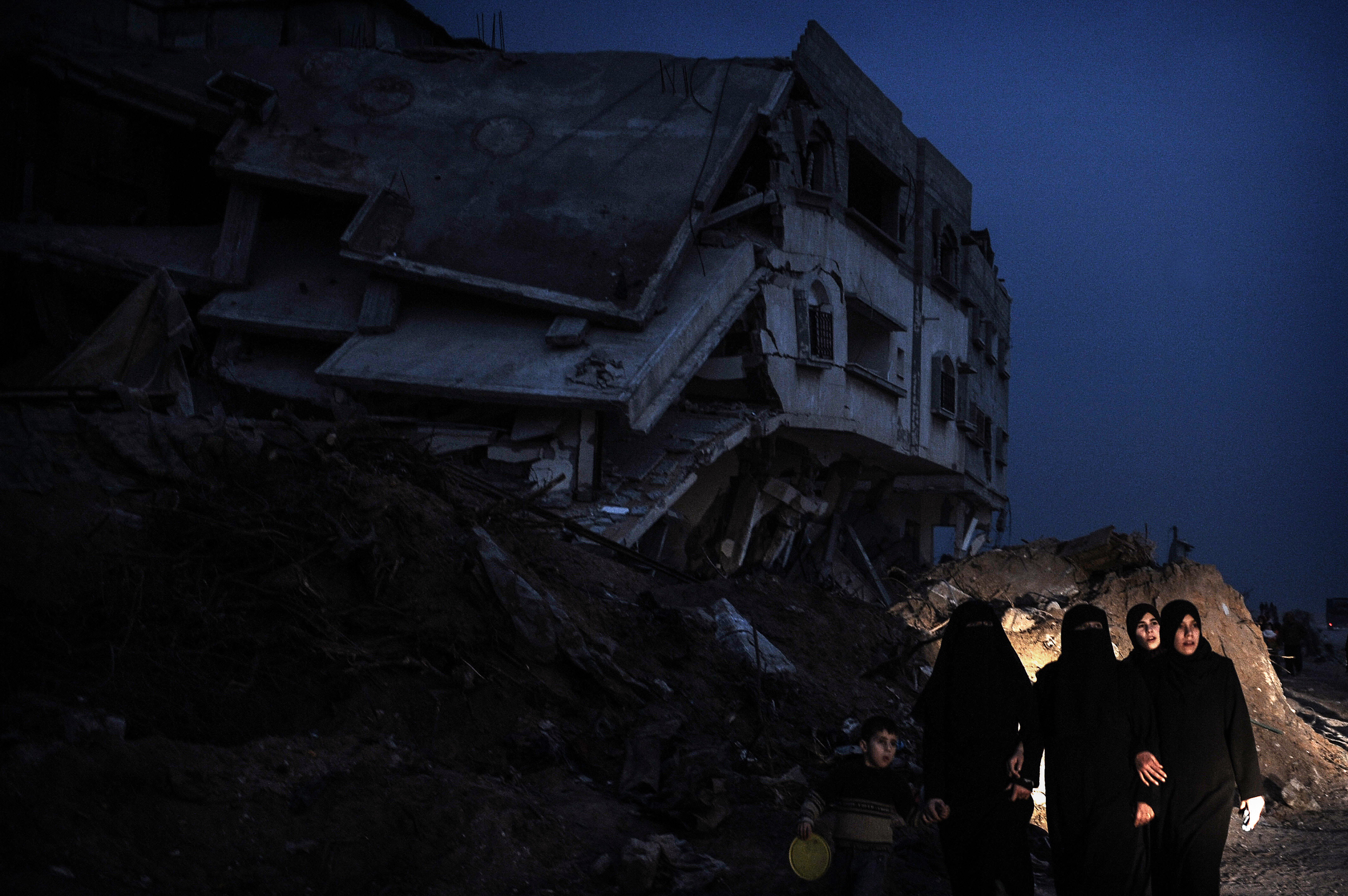 Palestinian women and a child walk past a destroyed house in the Israeli-bombed Jabalia in the northern Gaza Strip on January 23, 2009. A Hamas delegation from Gaza crossed into Egypt for talks to shore up the ceasefire with Israel which ended a 22-day assault on the coastal strip, a border official said. Israel and Hamas have observed their own ceasefires since January 18 when Israel ended Operation Cast Lead leaving a trail of devastation and 1,330 Palestinians dead, according to doctors. Egypt is trying to secure a durable ceasefire between Israel and Hamas and the reopening of crossings. AFP PHOTO/OLIVIER LABAN-MATTEI (Photo credit should read OLIVIER LABAN-MATTEI/AFP via Getty Images)